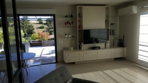 Ein modernes Wohnzimmer mit Fernseher, Regalen und einem Essbereich mit Tisch und Stühlen.