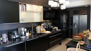 Eine moderne Küche mit schwarzen Schränken, einem Edelstahl-Kühlschrank, einer Kaffeemaschine und verschiedenen Küchengeräten.