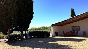 Un edificio con vialetto in ghiaia, un patio con mobili da esterno e un grande albero in primo piano.
