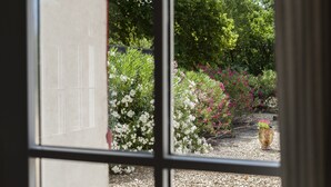Vista attraverso una finestra su un giardino con sentieri in ghiaia, diverse piante fiorite e una vasi decorativa.