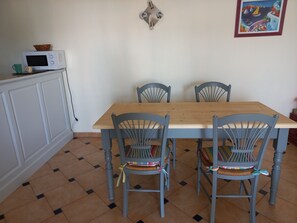 A dining area with a wooden table and four grey chairs, a microwave on a cabinet, and a colorful painting on the wall.