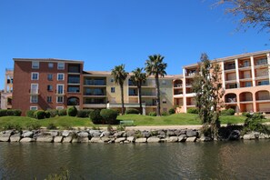 A multi-story hotel with balconies, a landscaped lawn, and a body of water in front.