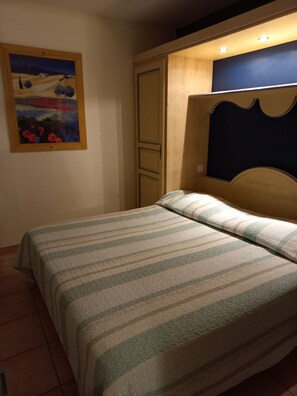 A bedroom with a bed, a wooden headboard, a painting on the wall, and a door.