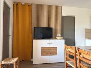 Ein Zimmer mit Fernseher auf einem weißen Schrank, einem Holzstuhl, einem gelben Vorhang und einer gestreiften Wandverkleidung.