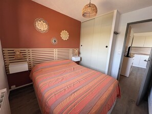 Um quarto com cama, guarda-roupa, mesa de cabeceira e luminária pendente.
