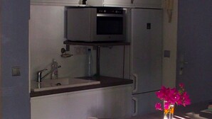A compact kitchen with a microwave, oven, and sink. There is a small table with a vase of flowers and a towel. - Bright apartment 80 meters from the lagoon, with large covered terrace (La Saline-Les-Bains)