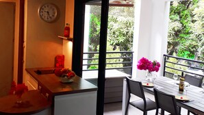 A dining area with a table set for two, a clock on the wall, and a view of greenery outside. - Bright apartment 80 meters from the lagoon, with large covered terrace (La Saline-Les-Bains)