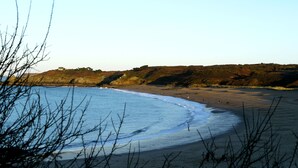 A beach with a clear sky, rocky cliffs, and a sandy shore. - Fisherman's house (Cancale)