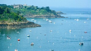 A coastal scene with a large building on a cliff, surrounded by greenery and rocky terrain. - Fisherman's house (Cancale)