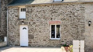 A stone building with a white door, a small window with a red frame, and a small balcony. - Fisherman's house (Cancale)