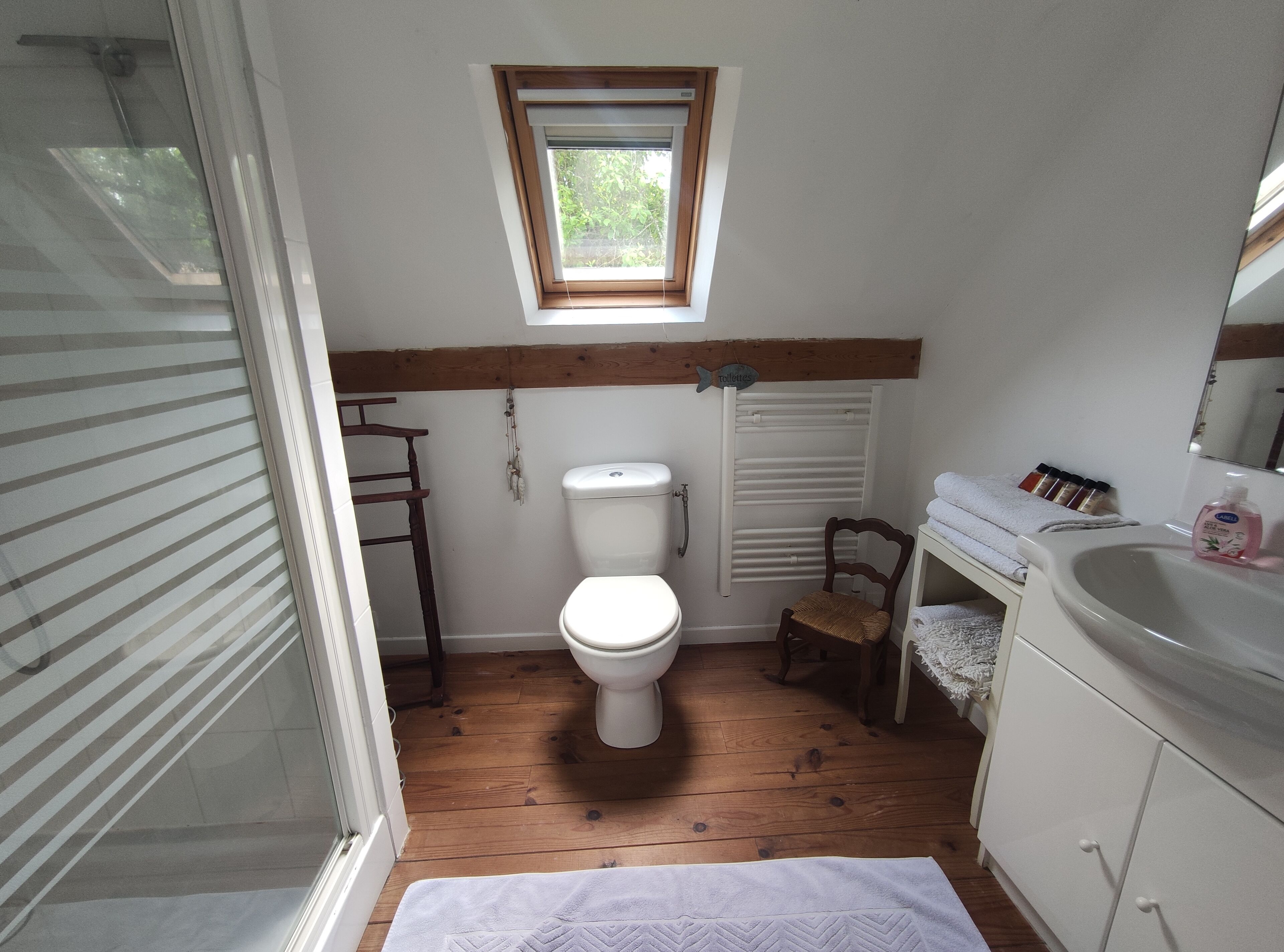 A small, compact bathroom with a toilet, a wooden chair, a small window, and a sink.