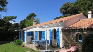 A house with a tiled roof, a stone wall, and a covered patio with a table and chairs.