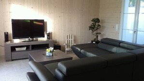 A modern living room with a sectional sofa, a flat-screen TV, a coffee table with a flower arrangement, and a potted plant. - La Fleur de Sel (La Flotte)