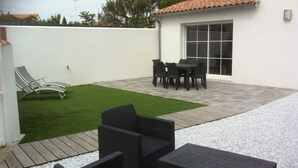 A patio with a small lawn, outdoor furniture, and a building with a tiled roof. - La Fleur de Sel (La Flotte)
