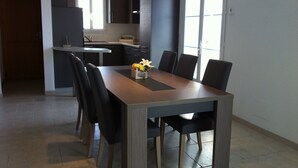 A modern kitchen with dark cabinets, a central island, and a dining area with a wooden table and black chairs. - La Fleur de Sel (La Flotte)