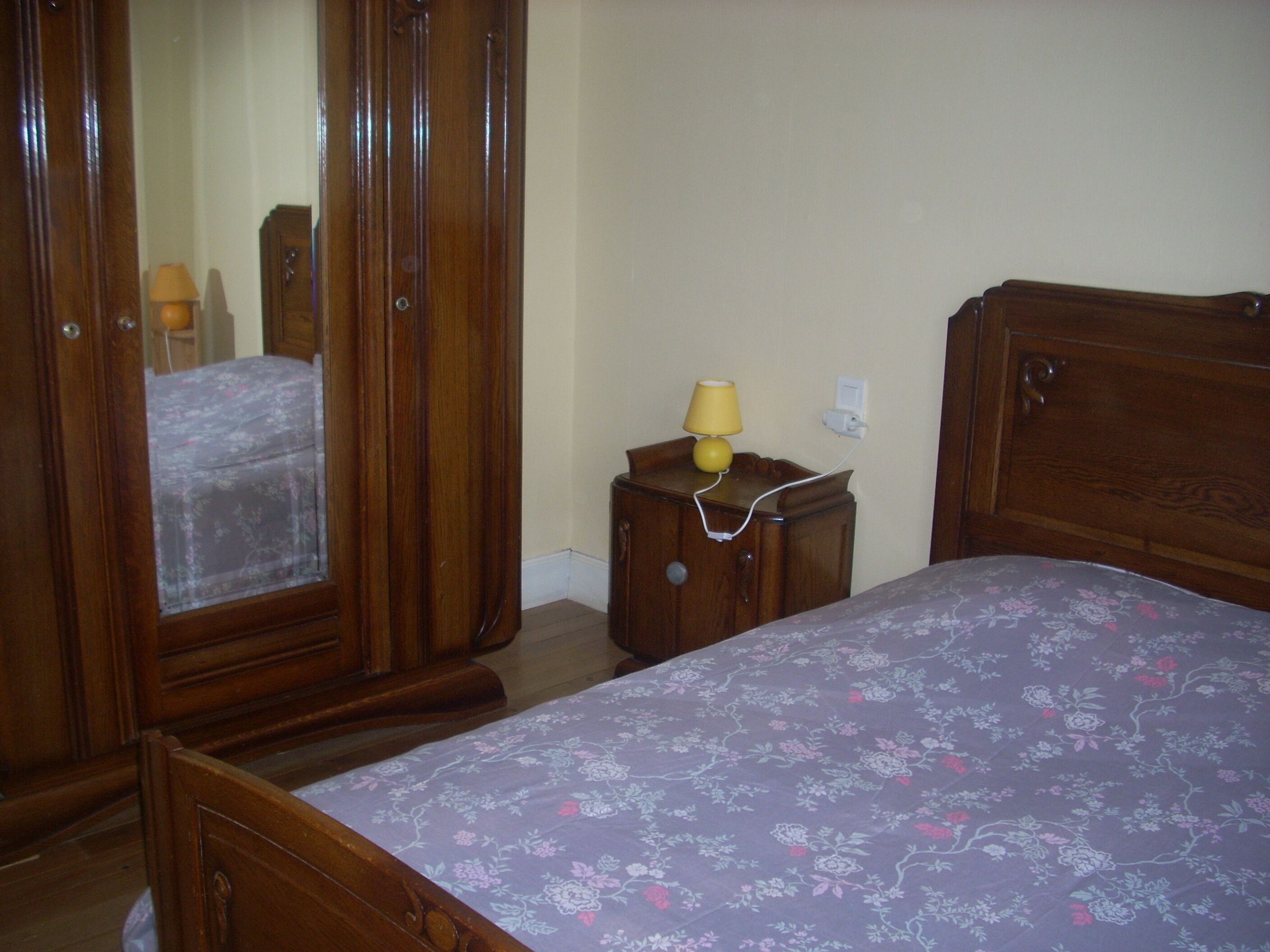 Een slaapkamer met een houten bed, een nachtkastje met een lamp en een garderobe.