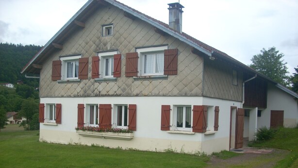 A two-story house with a sloped roof, multiple windows with shutters, and a small balcony with flowers. - 2-star detached holiday home (Rochesson)