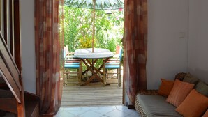 Une pièce comprenant un canapé, une table et une chaise. Il y a une fenêtre avec des rideaux, et de là, on peut admirer la verdure à l’extérieur.