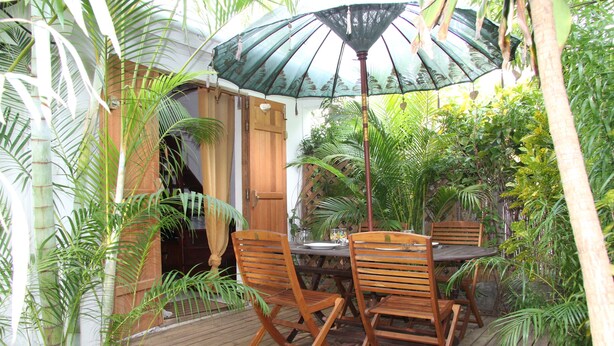 Une terrasse en bois avec une table et des chaises, entourée d’une végétation luxuriante et dotée d’une porte en bois.