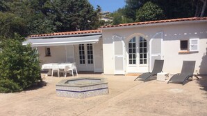 Une maison avec une terrasse carrelée, une petite piscine et deux chaises longues.