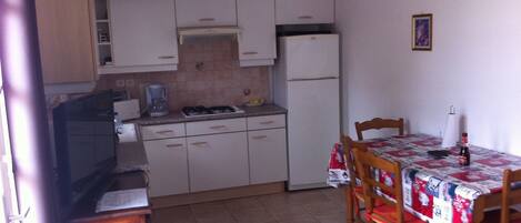 A compact kitchen with white cabinets, a gas stove, a refrigerator, and a dining table with chairs.