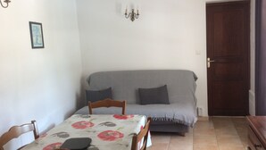 Une petite pièce agréable et chaleureuse, avec un canapé, une table à manger entourée de chaises, un luminaire fixé au mur et une porte en bois.