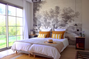 Ein Schlafzimmer mit großem Fenster, einem Bett mit gestreifter Bettwäsche und einer Baum-Mural an der Wand.