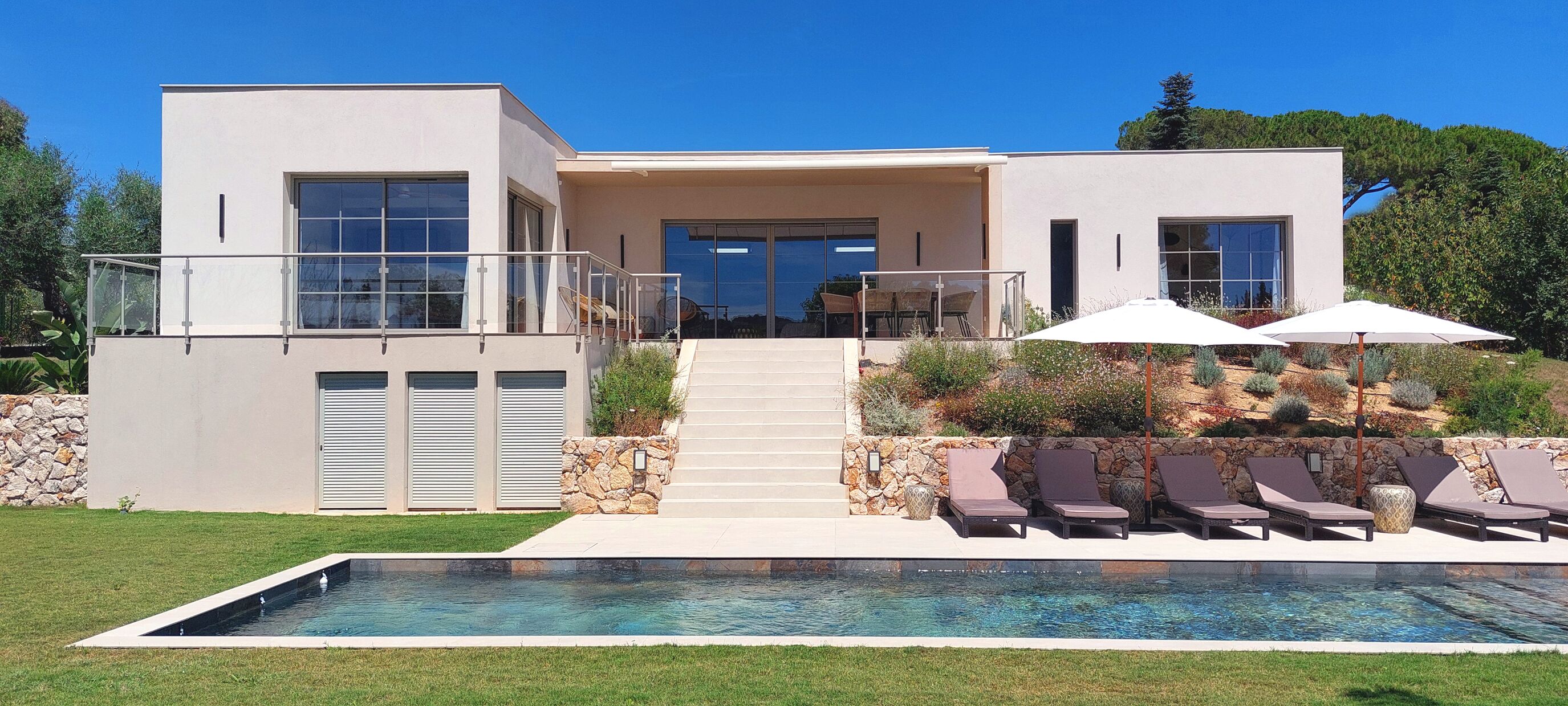 Una casa moderna de dos pisos con piscina, mobiliario exterior y un muro de piedra.