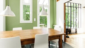 A dining area with a wooden table and white chairs, two pendant lights, and a view of greenery through large windows. - The charm of a family home in Tours (Tours)