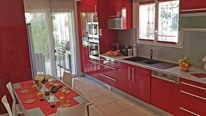A modern kitchen with red cabinets, a stainless steel sink, and a dining area with a table set for two. - Quiet villa Beach 10' walk Outdoor SPA Heated pool Boules court  (Saint-Cyr-Sur-Mer)