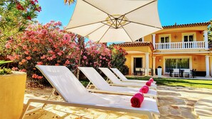 A poolside area with sun loungers, a large umbrella, and a two-story building with a balcony. - Quiet villa Beach 10' walk Outdoor SPA Heated pool Boules court  (Saint-Cyr-Sur-Mer)