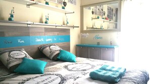 A bedroom with a bed, pillows, a bedside table, a mirror, and shelves with decorative items. - Quiet villa Beach 10' walk Outdoor SPA Heated pool Boules court  (Saint-Cyr-Sur-Mer)