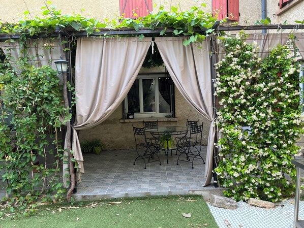 A patio with a table and chairs, a window, and a curtain.