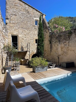 Un bâtiment en pierre doté d’une piscine, de mobilier d’extérieur et de plantes en pot.
