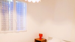 Una camera da letto con un letto, un comodino, una lampada e una finestra con tende a motivi.