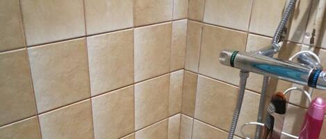 A bathroom with beige tiles, a white bathtub, and a shower with a metal rack holding toiletries.