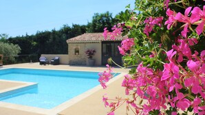 A swimming pool with a clear blue water, surrounded by a beige tiled deck. In the background, there is a small building with a tiled roof and a potted plant. - CHARMING GITE IN PROVENCE / MERINDOL IN LUBERON (Mérindol)
