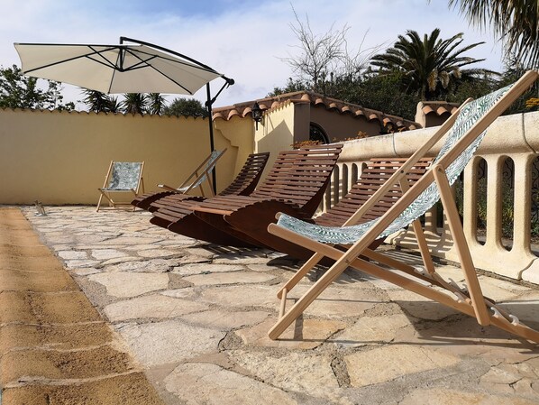 A patio with stone flooring, wooden lounge chairs, and a white umbrella. - Bastide "villa cinnamon 'Agde - downtown (Agde)
