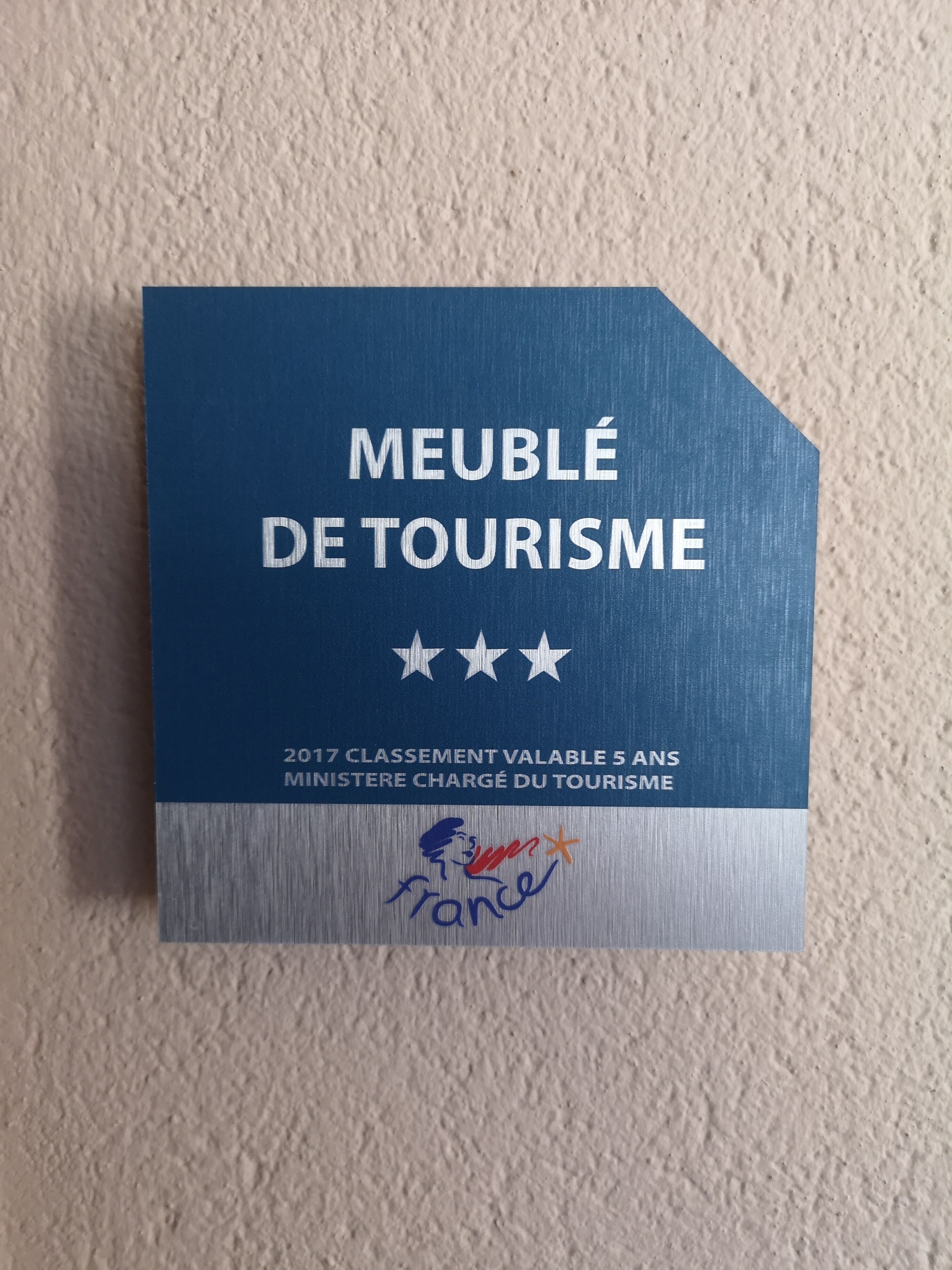 Une plaque bleue, ornée d’un texte et d’un logo, fixée à un mur à texture.