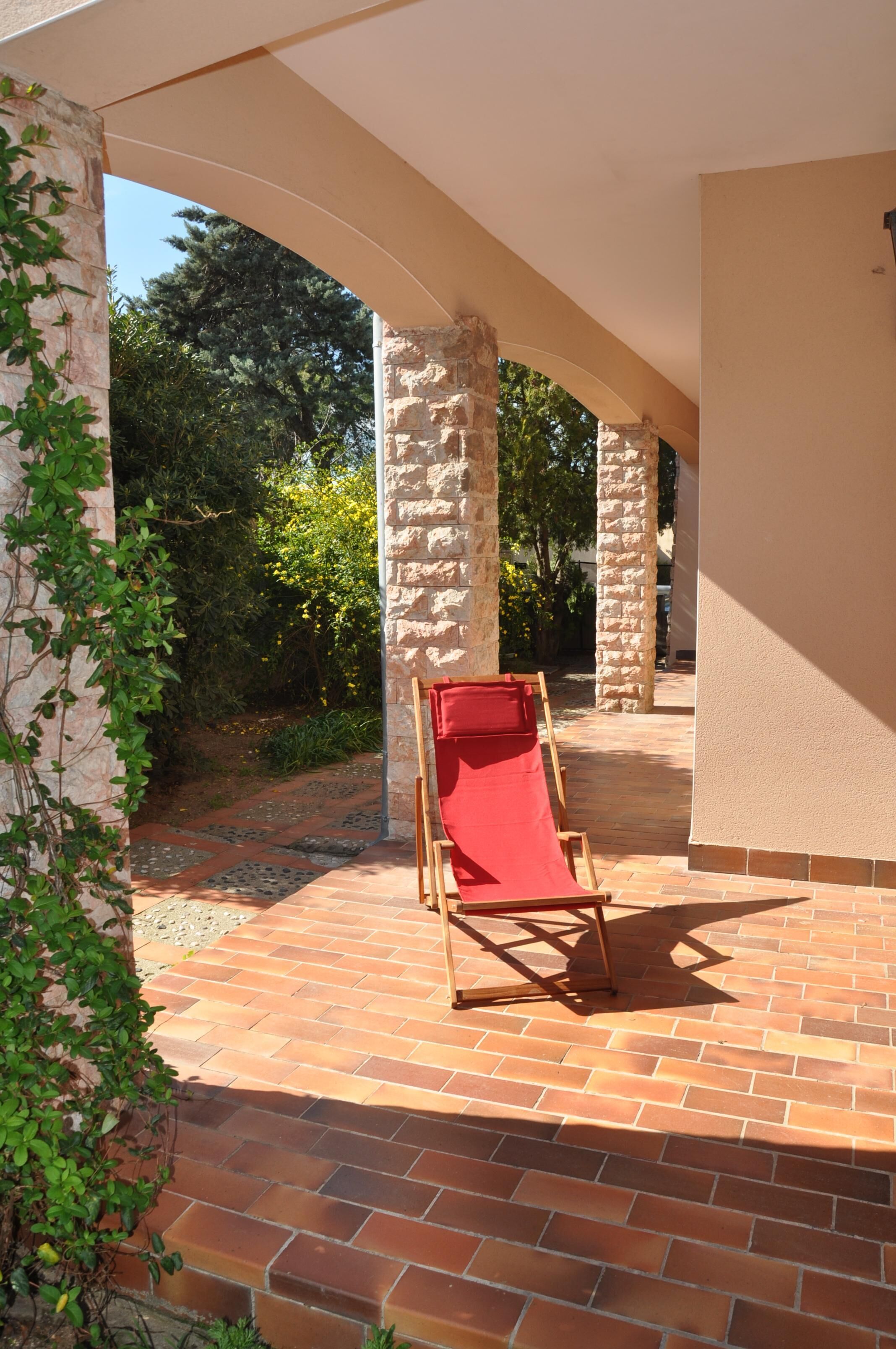 Un patio couvert avec un sol en briques, une chaise rouge et des piliers en pierre.