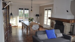 Een moderne woonkamer met een grijze bank, een eettafel met stoelen en een open haard.