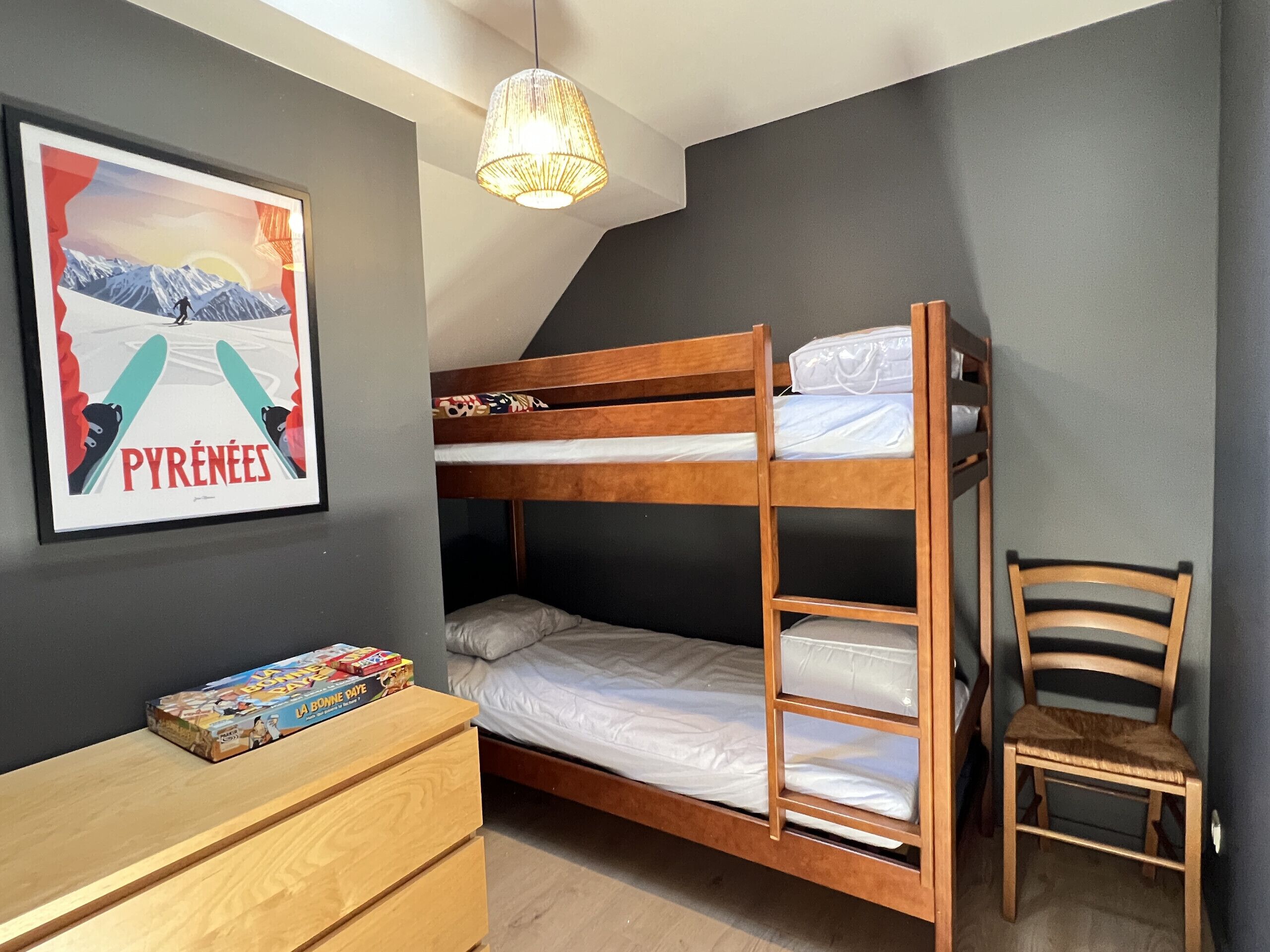 Habitación con literas, un cuadro en la pared, un aparador de madera y una silla.