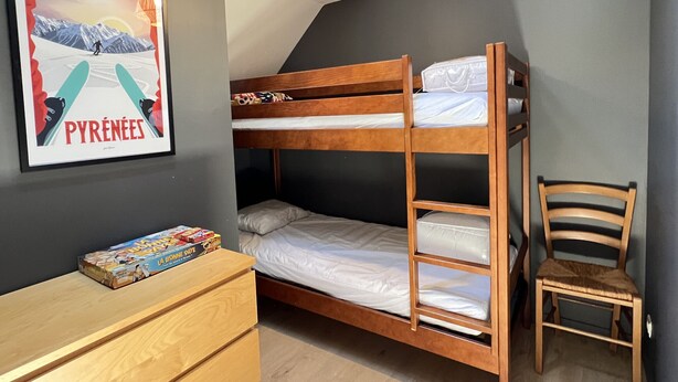 Une chambre avec un lit superposé, un tableau encadré au mur, une commode en bois et une chaise.
