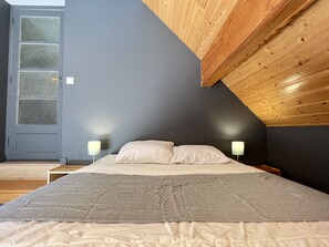 Une chambre à coucher avec un lit, deux lampes de chevet, un mur gris et un plafond en pente en bois.