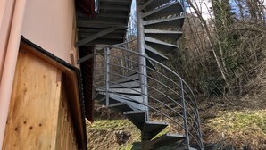Un escalier en colimaçon menant à l’étage supérieur d’un bâtiment, entouré d’arbres et surplombant un ciel dégagé.