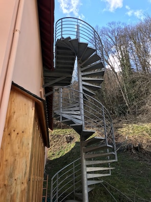 Un escalier en colimaçon menant à l’étage supérieur d’un bâtiment, entouré d’arbres et surplombant un ciel dégagé.