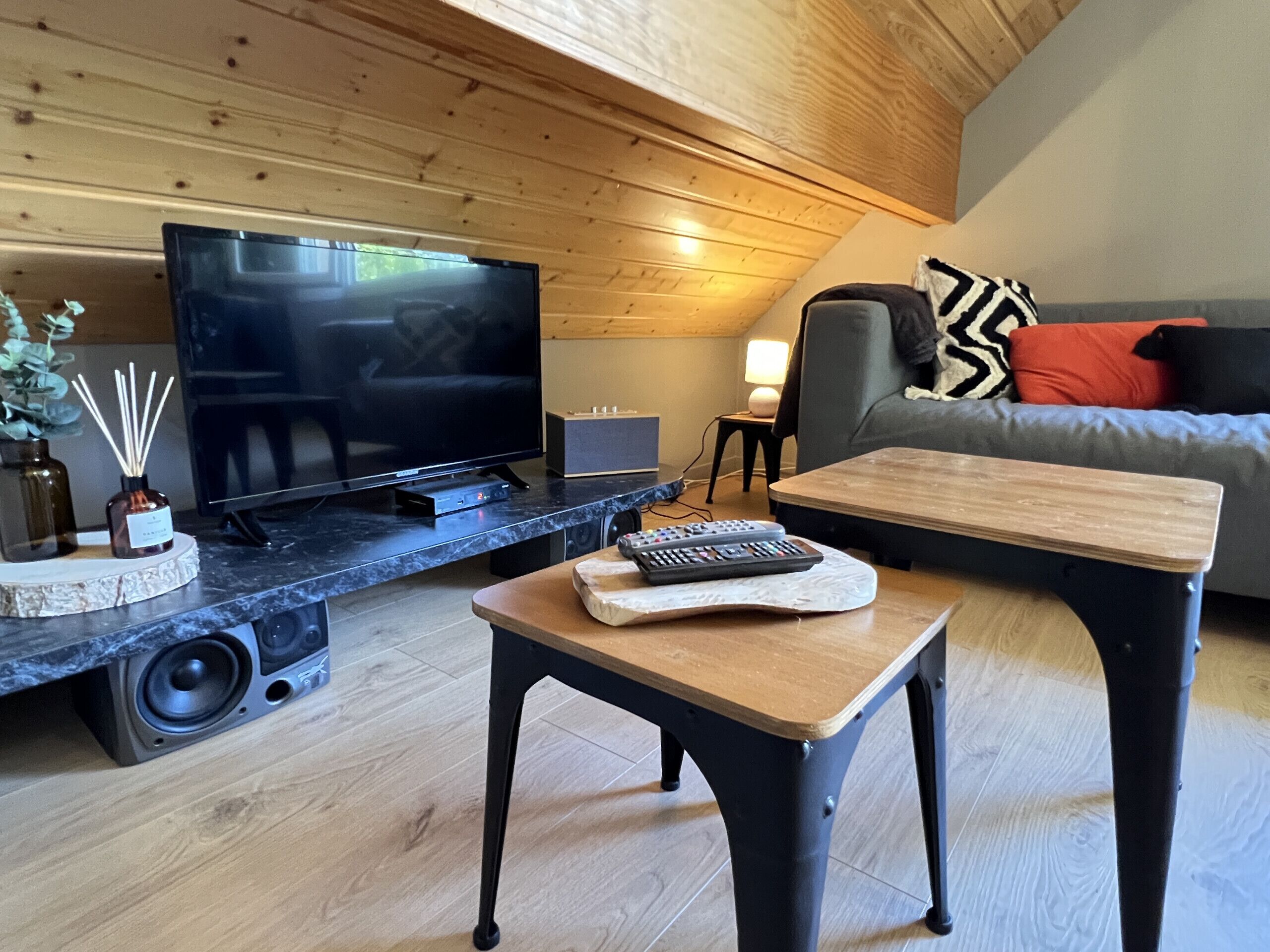 A modern living room with a flat-screen TV, a coffee table, a sofa, and a wooden ceiling.