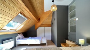 Une chambre avec un plafond en pente, un puits de lumière, un lit avec une tête de lit blanche, une table de chevet, une lampe et une armoire.
