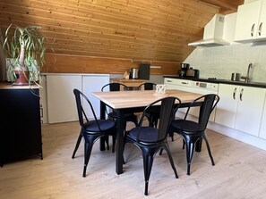 Une cuisine moderne avec un plafond en bois, des armoires blanches et une table à manger entourée de chaises noires.
