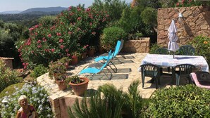 An outdoor patio with stone flooring, a table with a patterned tablecloth, and blue chairs. - Ground floor, 4p, swimming pool, air conditioning, mature garden, wide sea view near Fautéa beaches (Zonza)